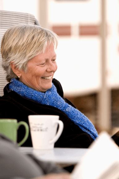 Older woman laughing with coffee mugs nearby